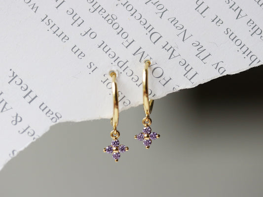 Shan&Co's Gold Vermeil Four Leaf Clover Purple CZ Dangle Huggies Earrings, featuring a delicate four-leaf clover charm adorned with purple crystal zirconia, perfect for adding a touch of elegance and luck to any outfit.